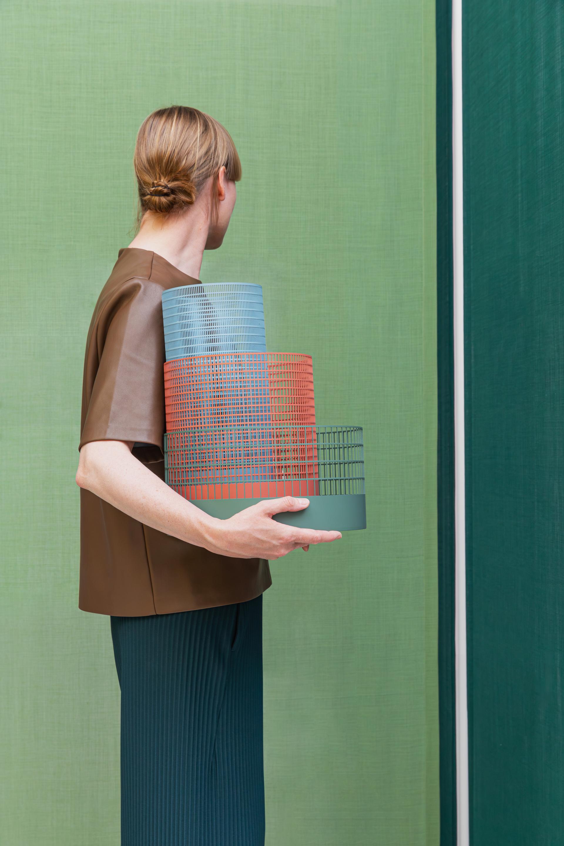 A person holding stacked bio-based color palettes against a green backdrop, reflecting on sustainable material design.
