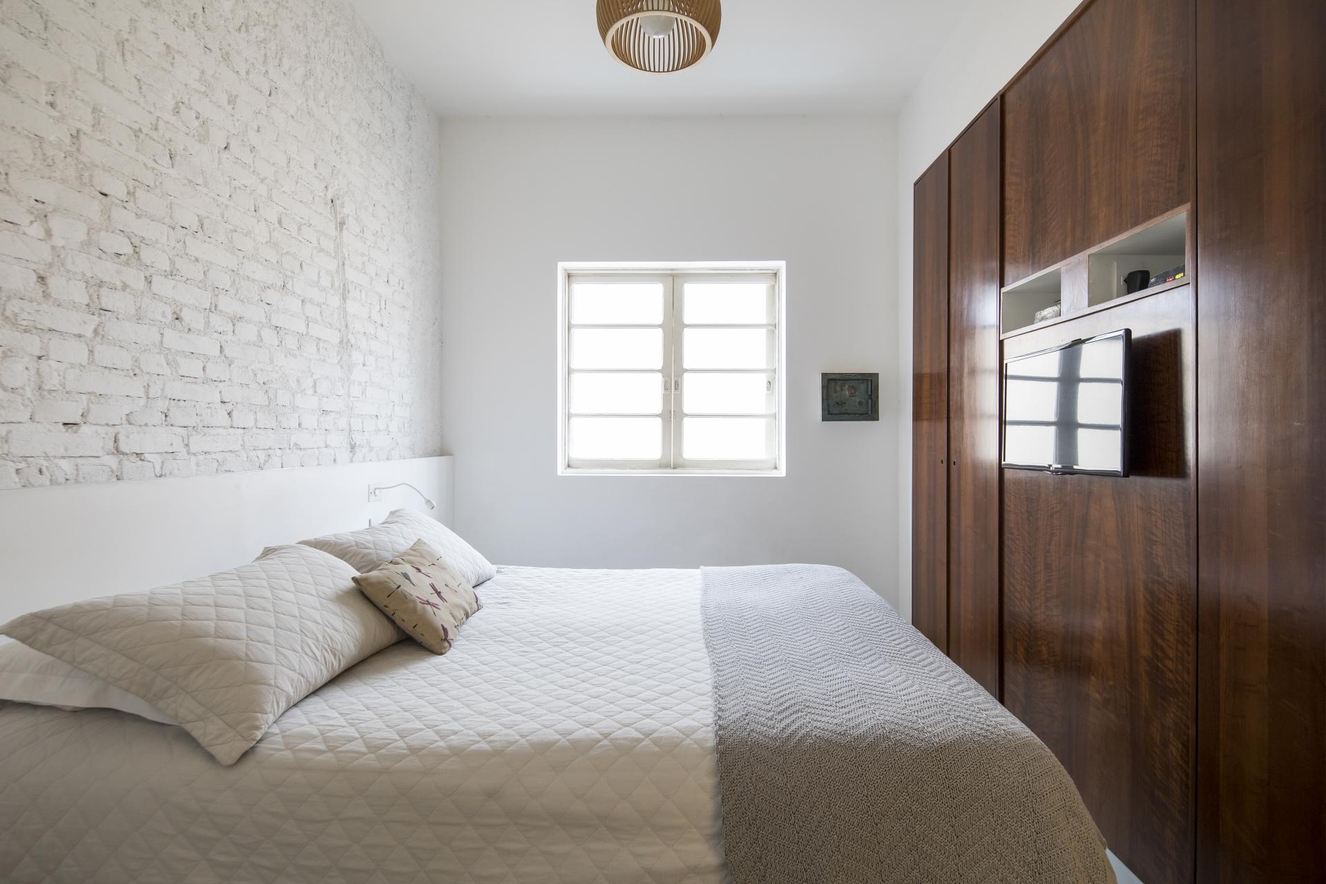 Renovated mid-century bedroom in São Paulo featuring a white brick wall, modern furniture, and natural light.
