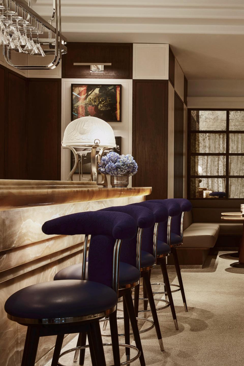 Elegant bar scene with plush navy stools, modern decor, and a floral centerpiece at The Maybourne Bar.
