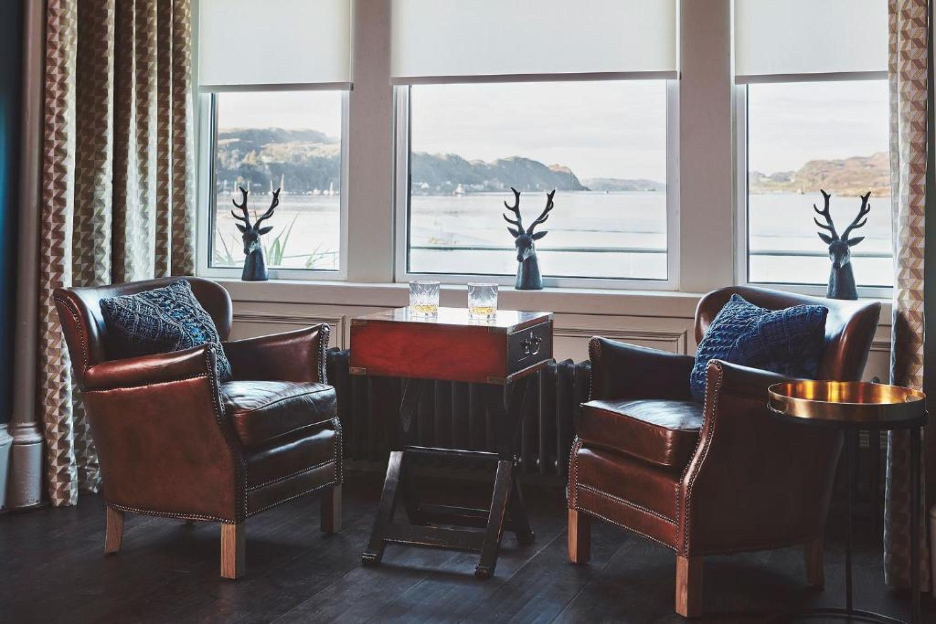 Chic lounge area in Oban hotel featuring leather armchairs, modern decor, and scenic coastal views through large windows.