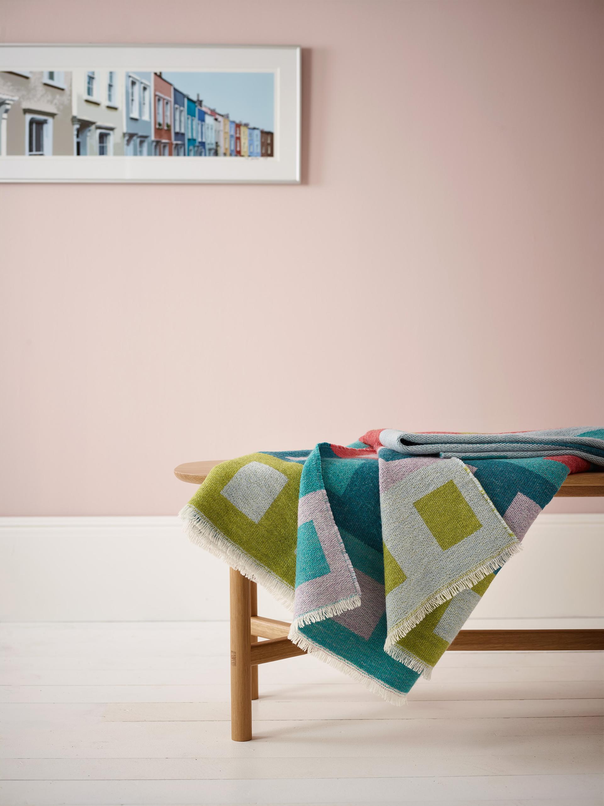 Colorful geometric-patterned blanket draped on a wooden bench, with pastel-colored walls and art showcasing Bristol's vibrant architecture.