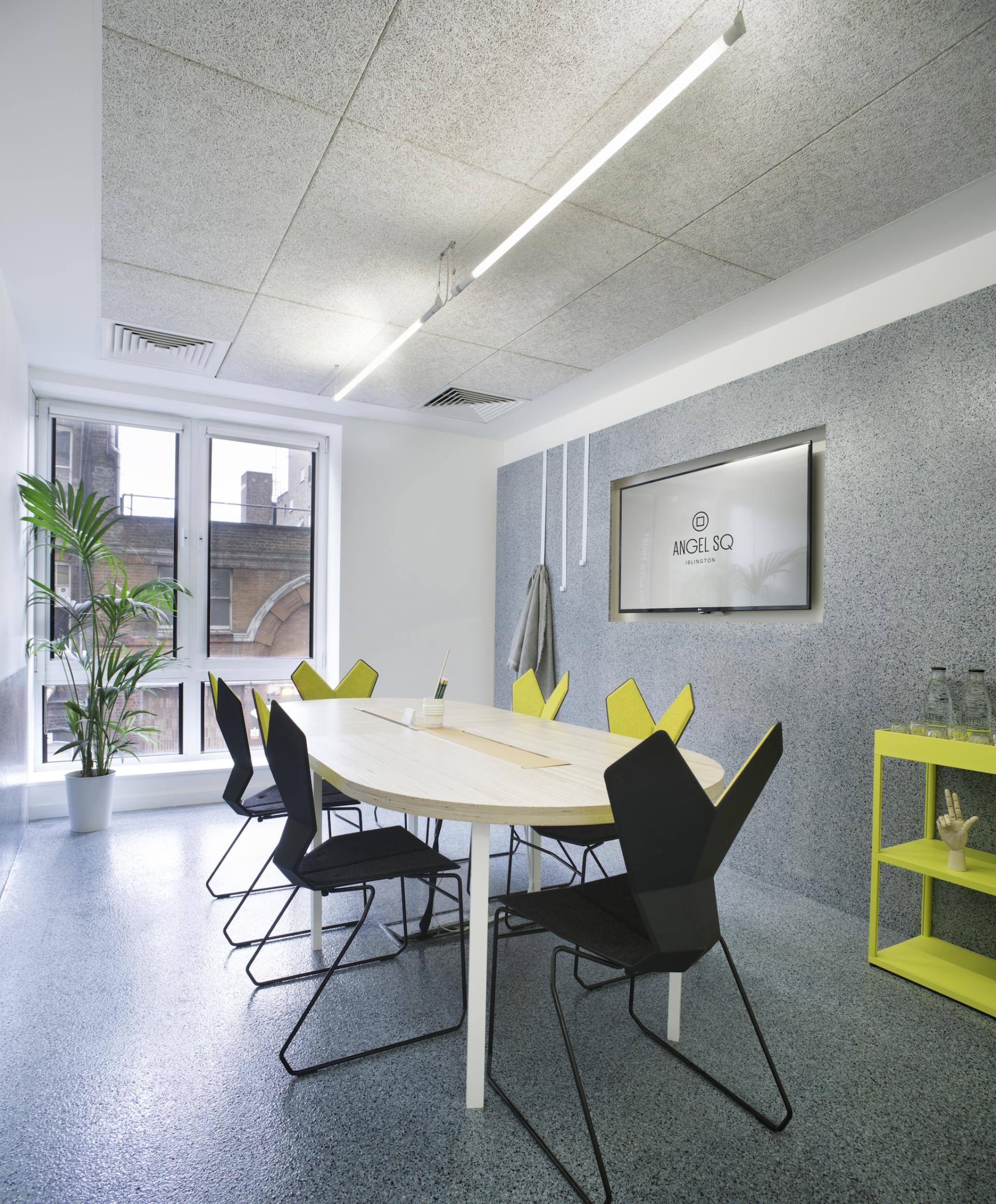 Modern workspace at 2 Angel Square featuring a stylish oval table, black chairs, and a vibrant yellow accent wall.
