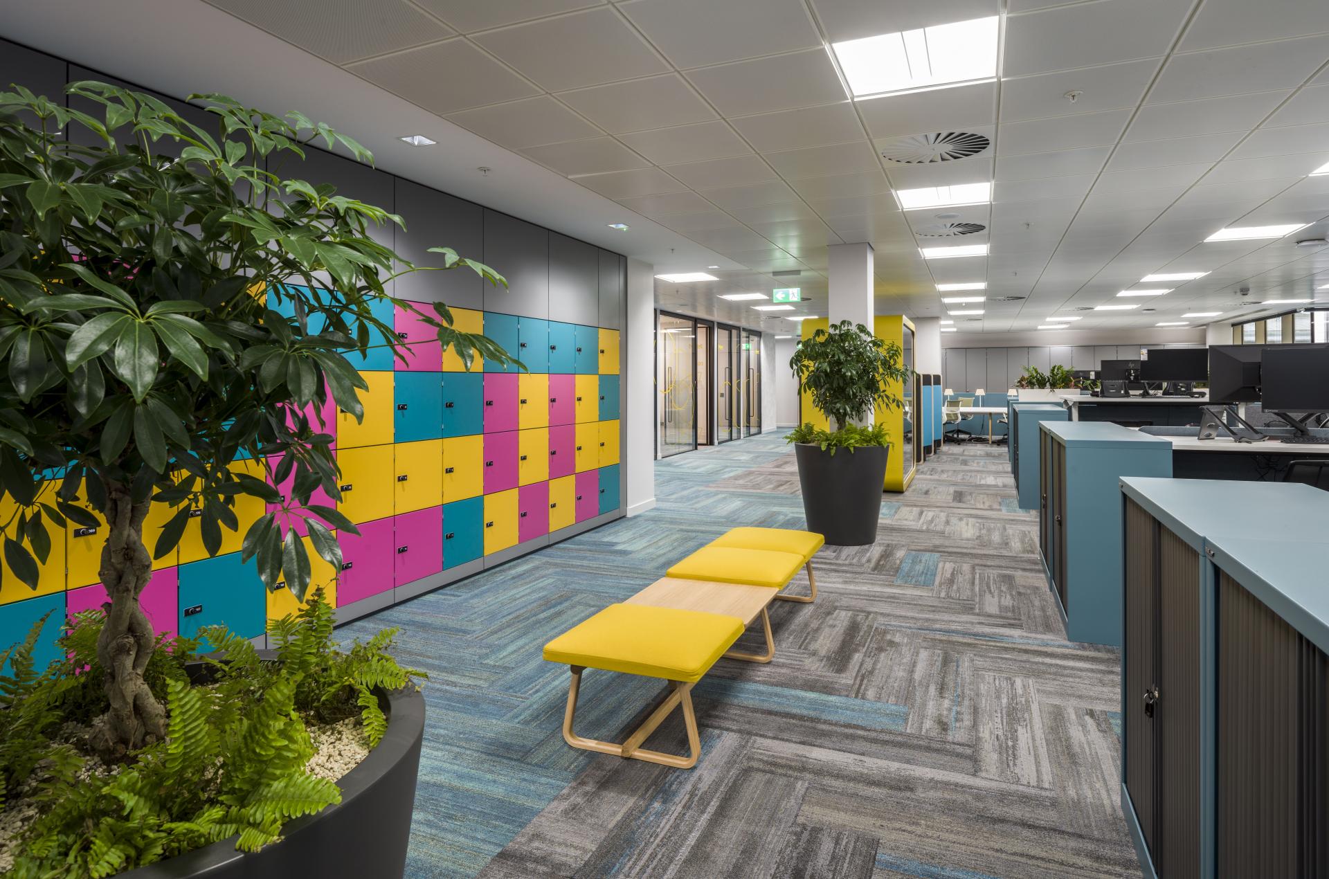 Vibrant office interior featuring colorful lockers, greenery, and contemporary furniture, highlighting WELL certification principles in design.