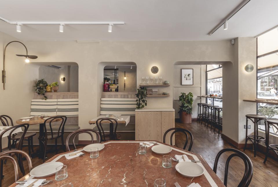 Modern interior of Honey & Co Bloomsbury featuring wooden furnishings, elegant marble tables, and lush greenery.