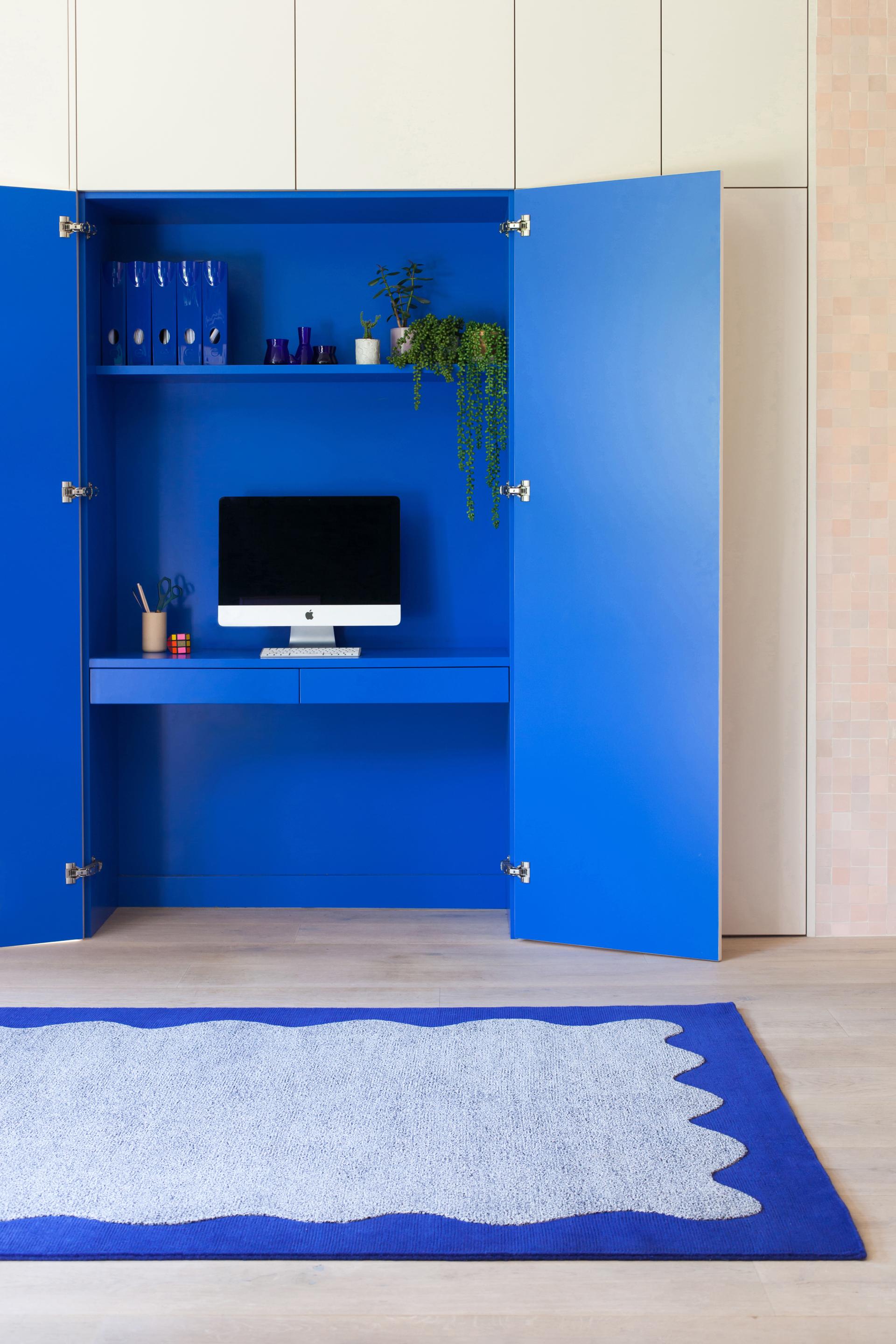 Vibrant blue cupboard reveals a modern workspace with an iMac, surrounded by a stylish rug from the 2LG Studio x FLOOR_STORY collection.