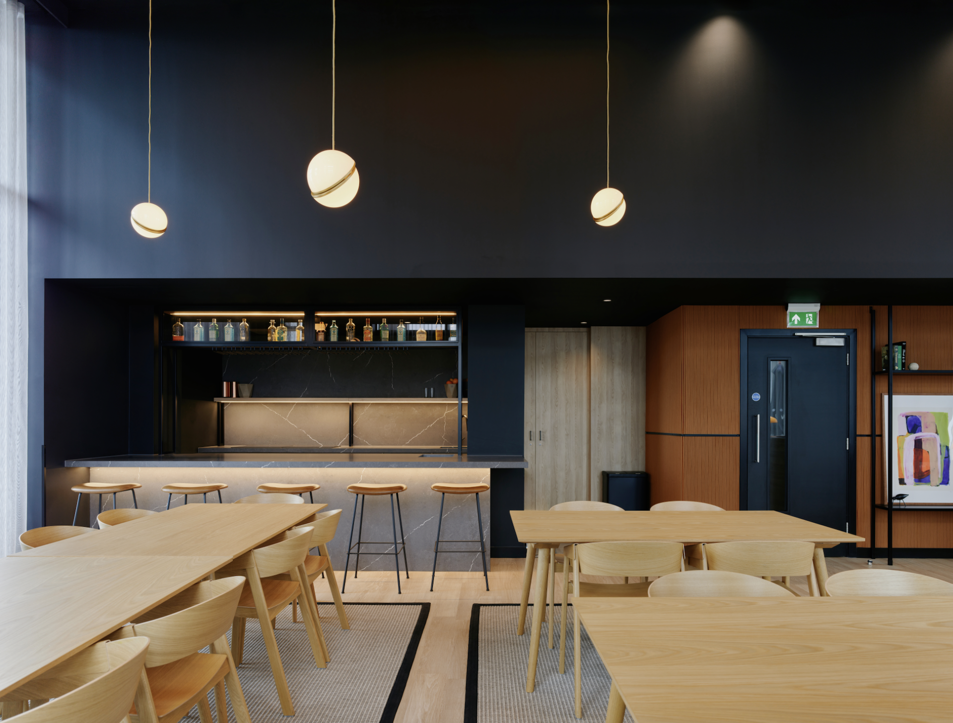 Modern communal space featuring wooden tables, stylish bar with illuminated shelves, and contemporary decor reflecting Vita Group's uhaus brand.