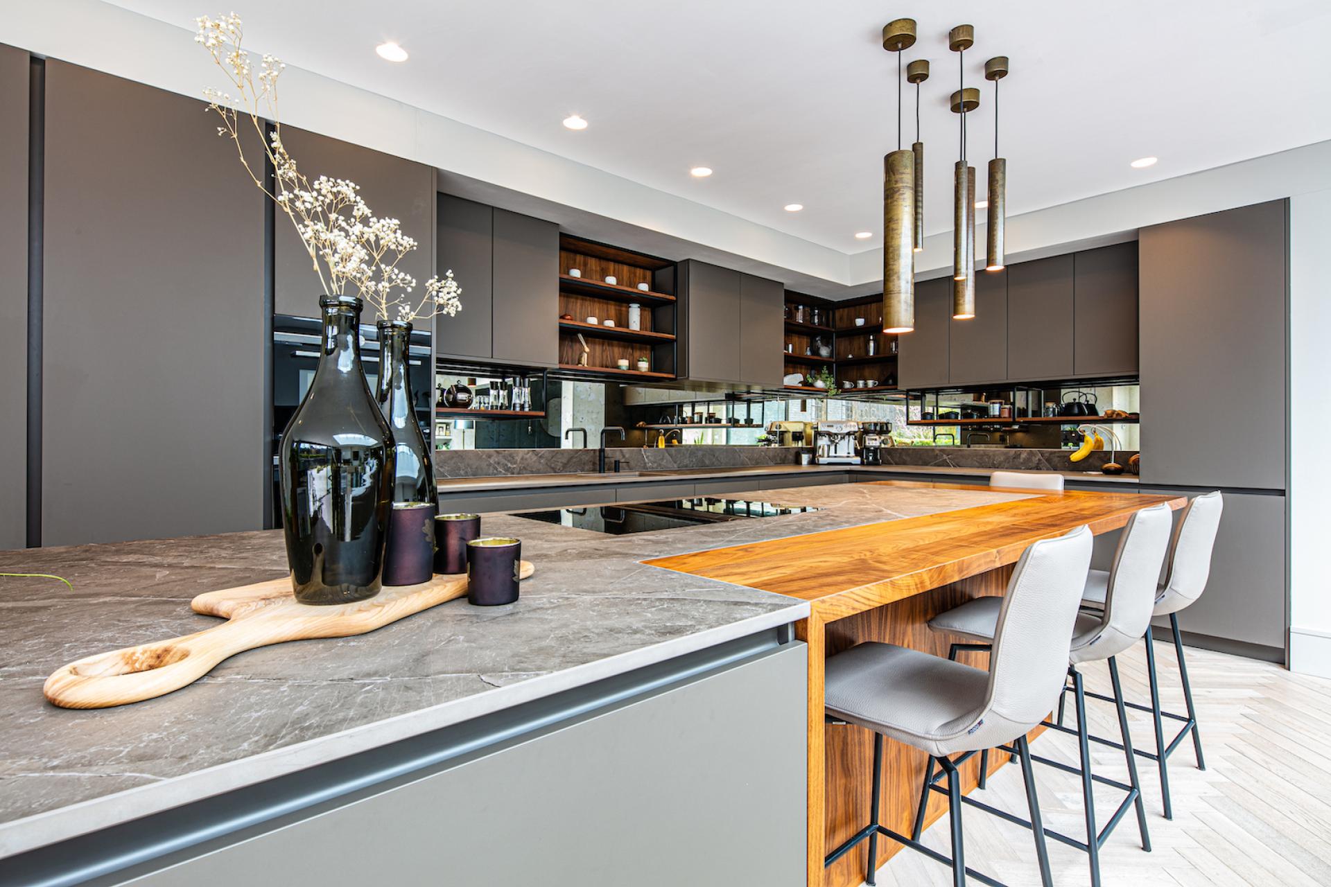 Modern kitchen showcasing contrasting surfaces of Dekton countertop and wooden breakfast bar, with stylish decor elements and ample storage.