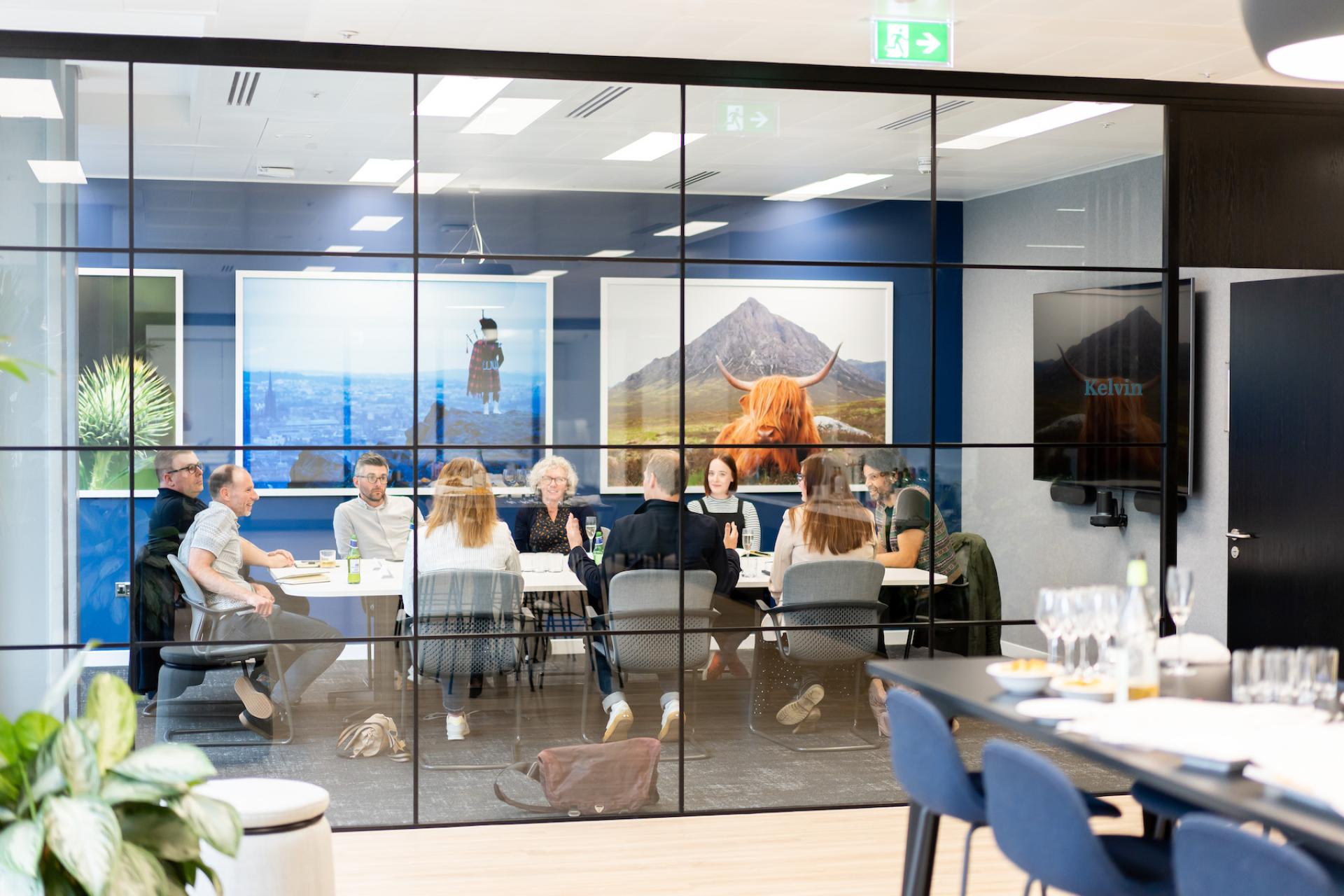Modern workplace meeting with diverse professionals collaborating in a glass-walled conference room, showcasing innovative design.