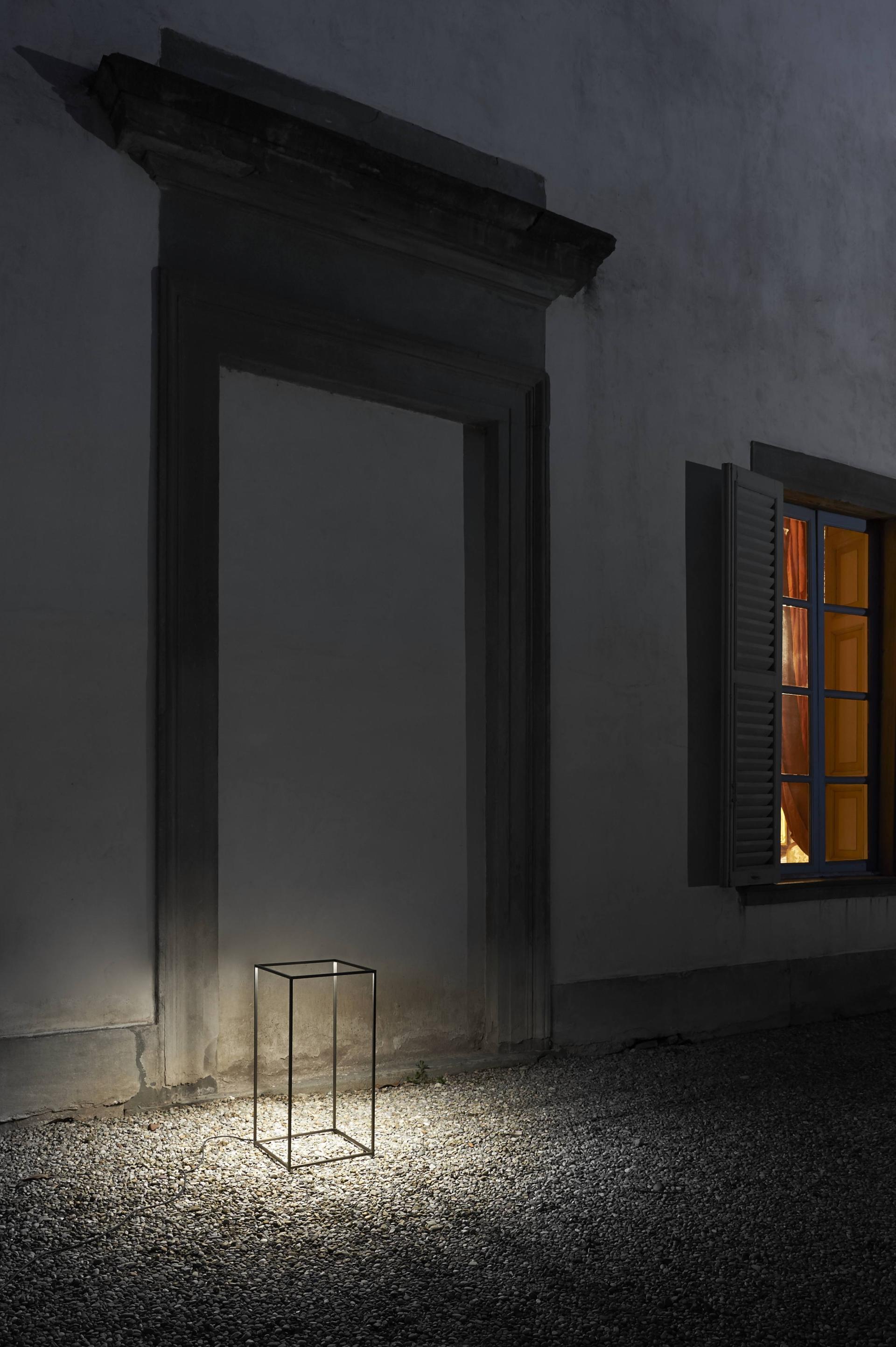 Sleek portable outdoor lamp illuminating a gravel path beside a building with a window at night.