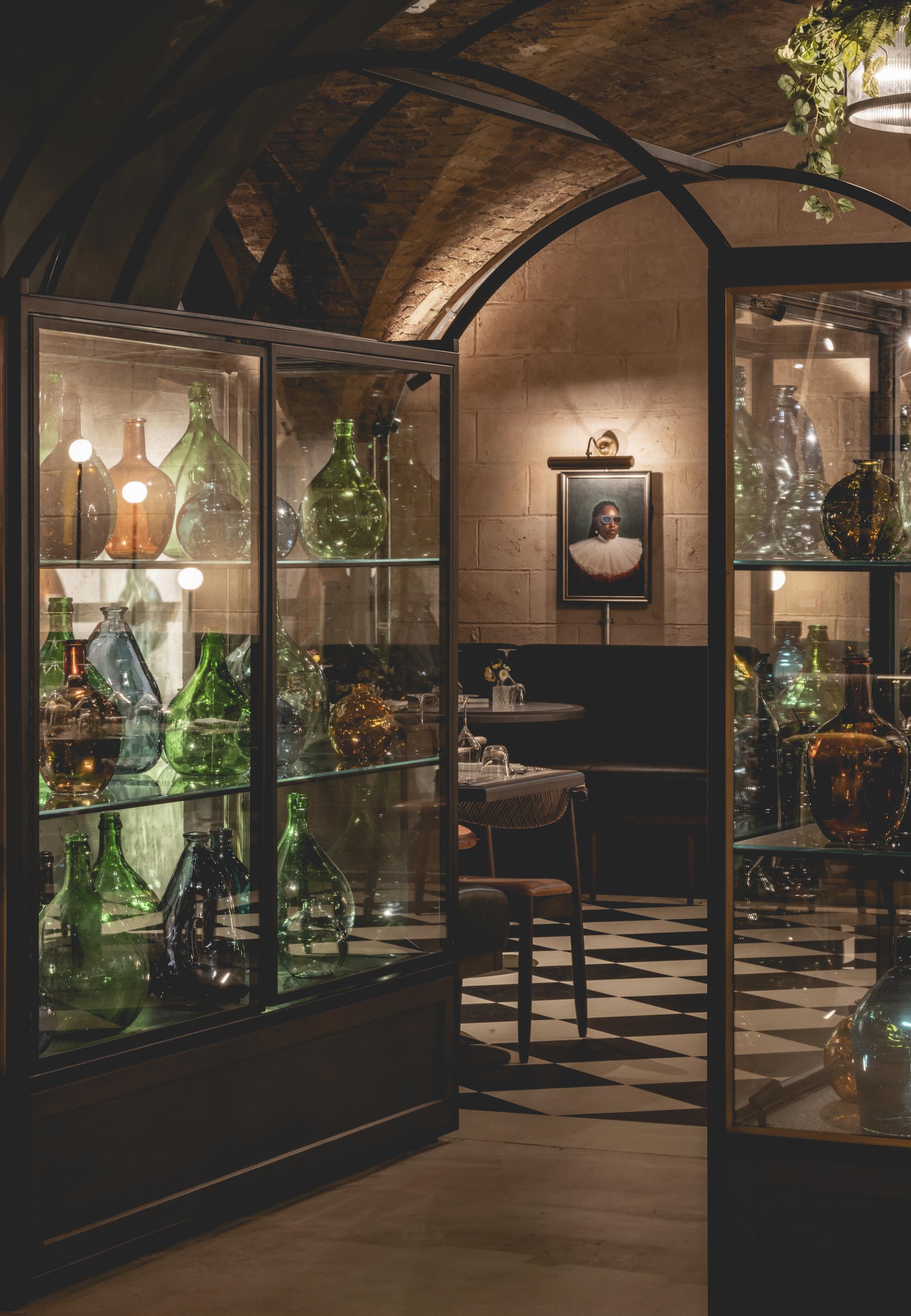 Interior view of The Libertine, showcasing colorful glass bottles and an elegant dining area in the Royal Exchange.