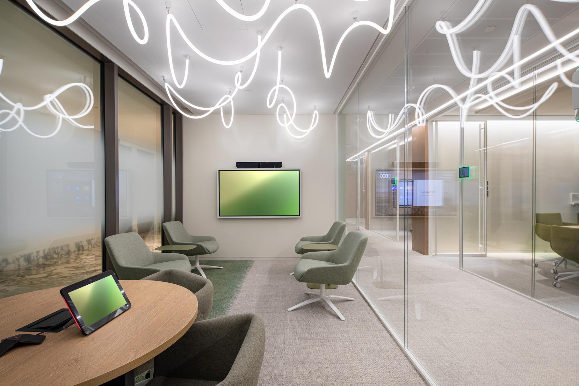 Modern office space in Dubai featuring vibrant ceiling lighting, green seating, and a display screen, emphasizing a nature-inspired design.
