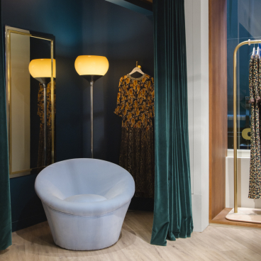 Stylish interior of Rixo's Carnaby store featuring a vintage chair, decorative clothing, and elegant lighting.