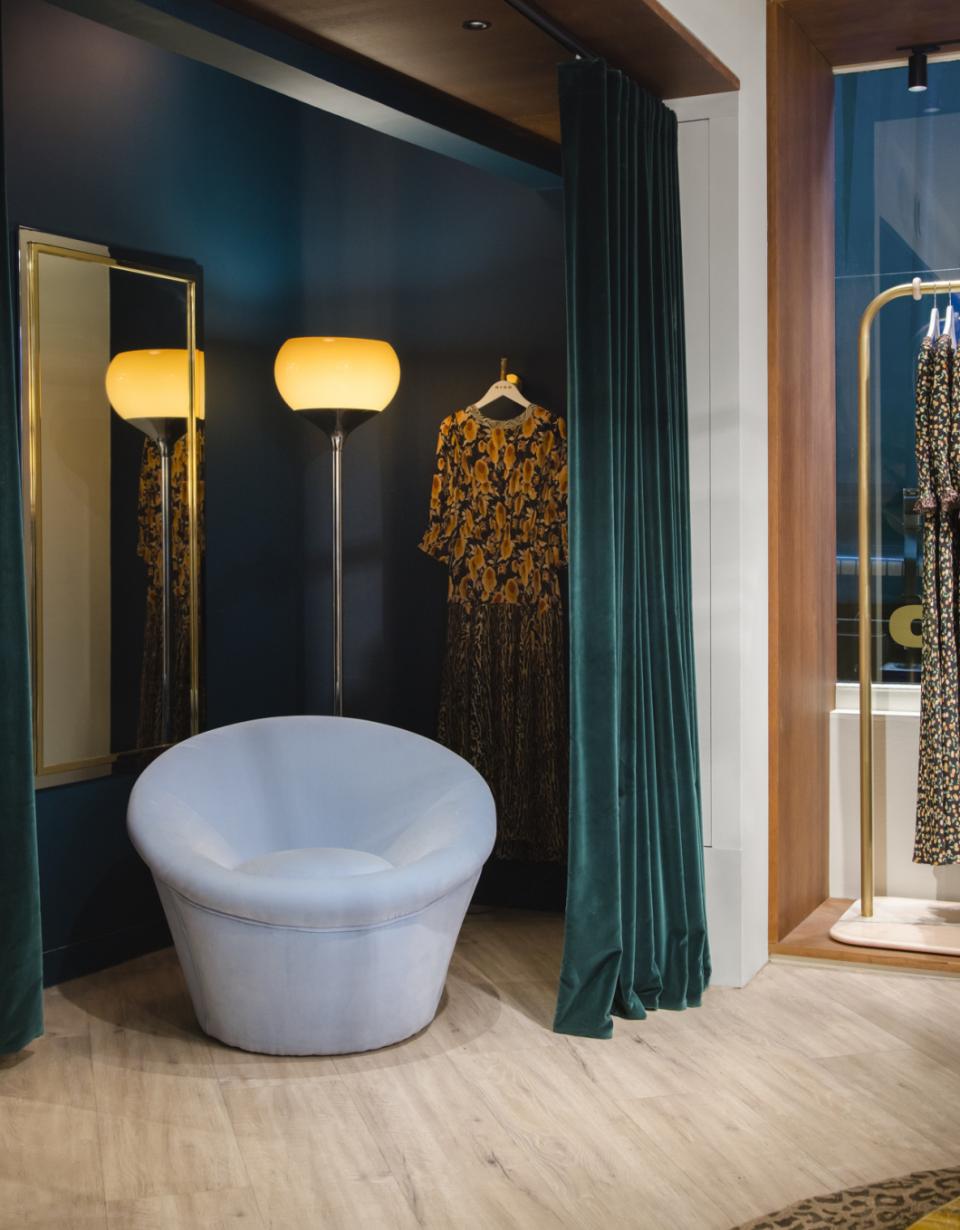 Stylish interior of Rixo's Carnaby store featuring a vintage chair, decorative clothing, and elegant lighting.
