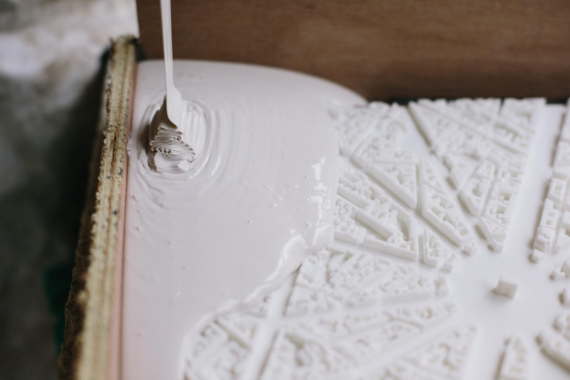 White resin being poured onto a detailed three-dimensional city model, showcasing urban landscape design techniques.