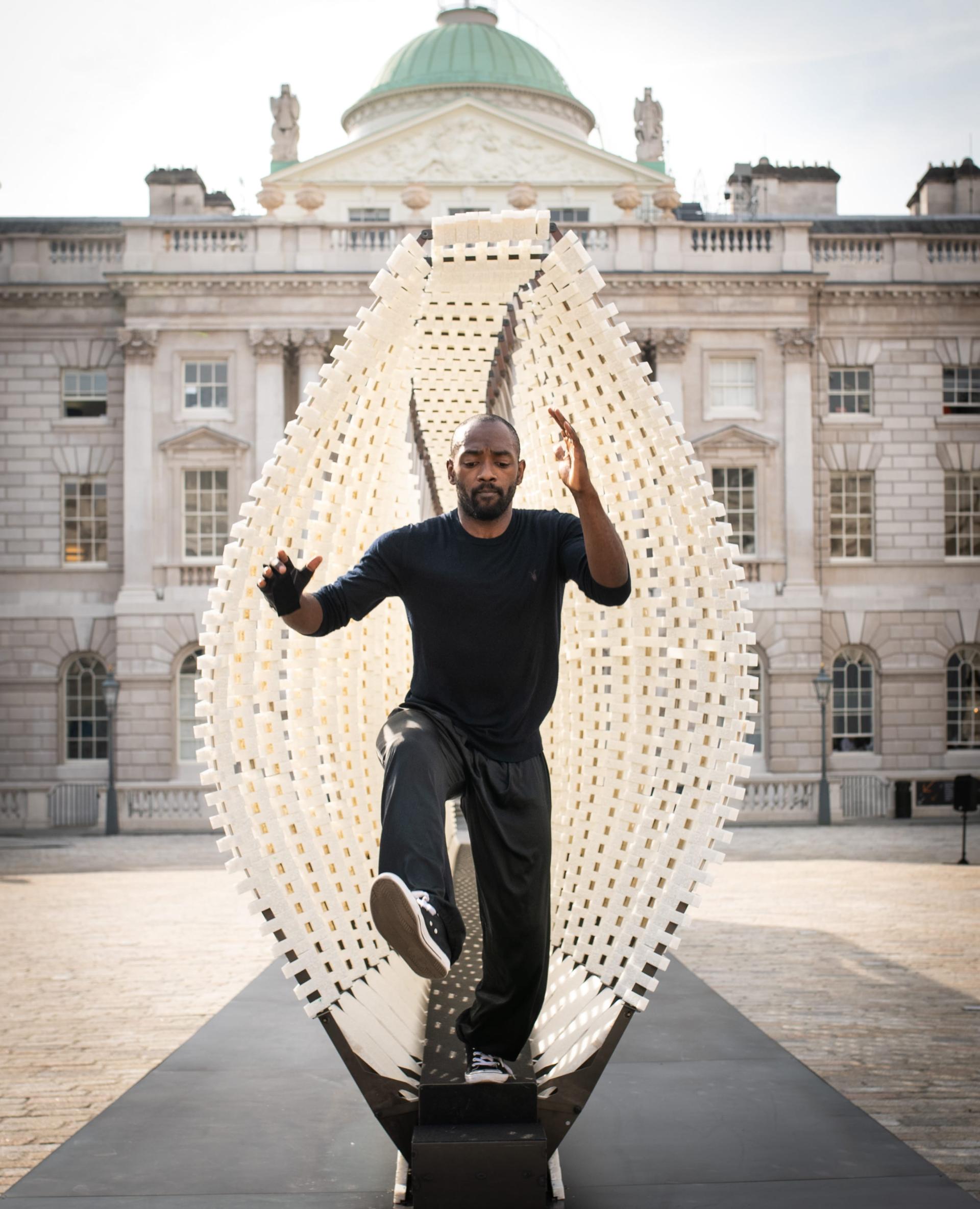 A performer engages in a dynamic pose within a striking white sculpture at the London Design Biennale, Somerset House.