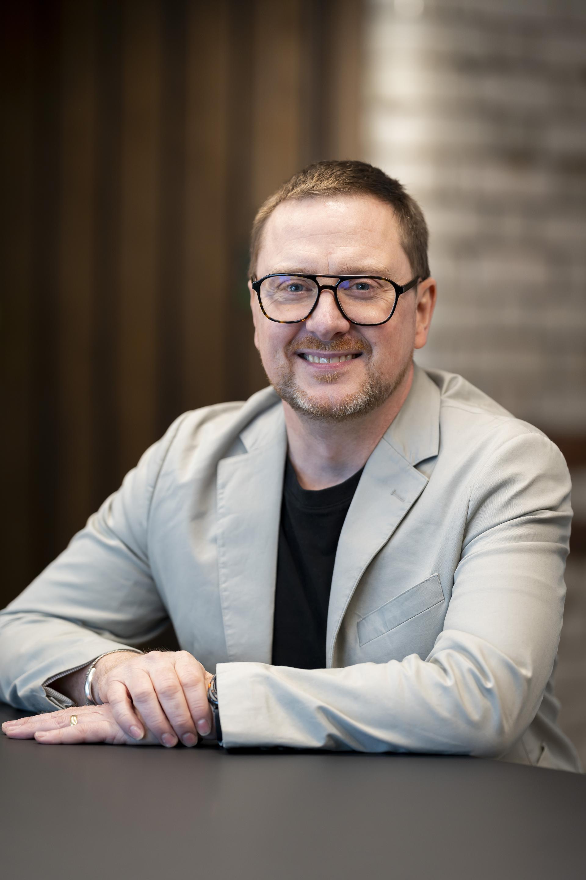 Senior design professional discusses technology's role in sustainability, seated at a table in a modern workspace.