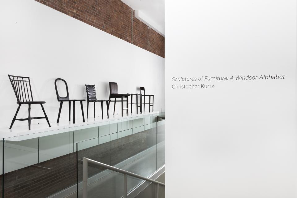 Windsor chairs displayed on a glass shelf, showcasing Christopher Kurtz's reinterpretation of iconic 18th-century furniture.
