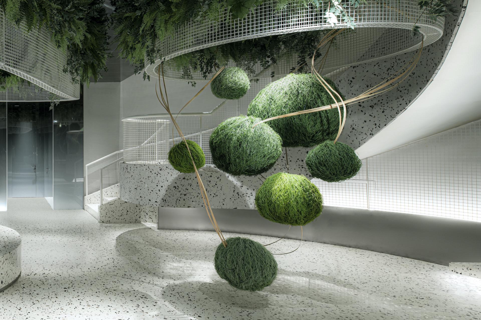 Modern café interior featuring terrazzo flooring, curved mesh grids, and suspended green moss spheres for a fresh ambiance.