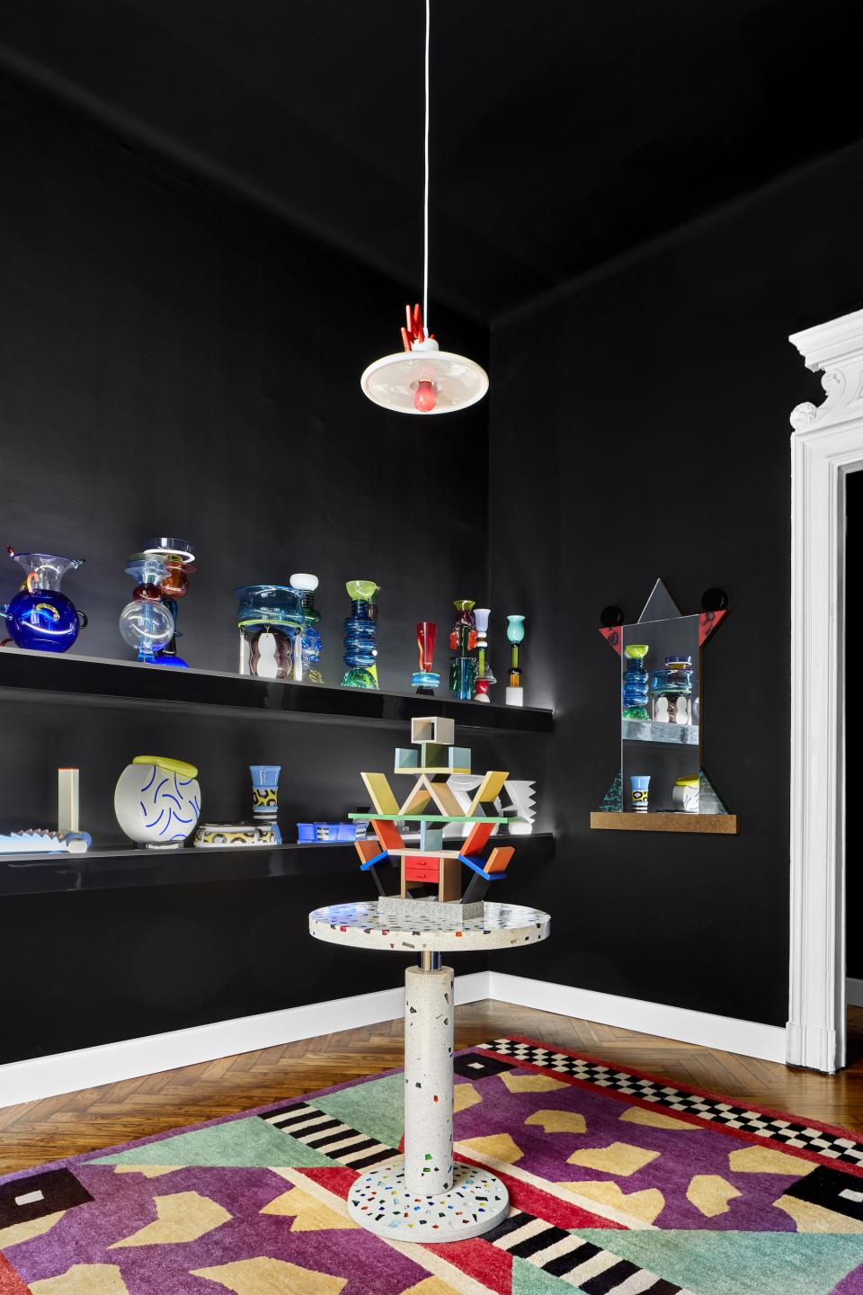 Colorful Memphis Milano furniture and decorative items displayed against black walls, showcasing contemporary design aesthetics.