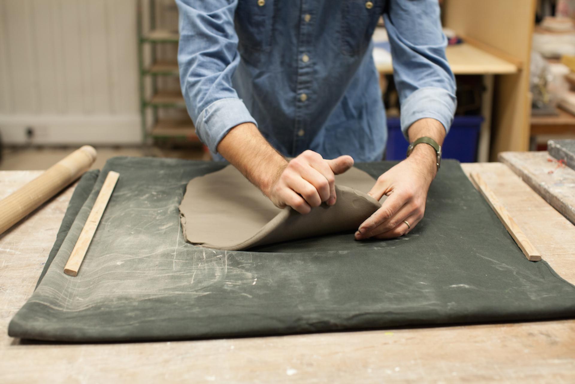 Ceramic artist manipulating soft clay on a work surface, exploring textural possibilities in contemporary art.