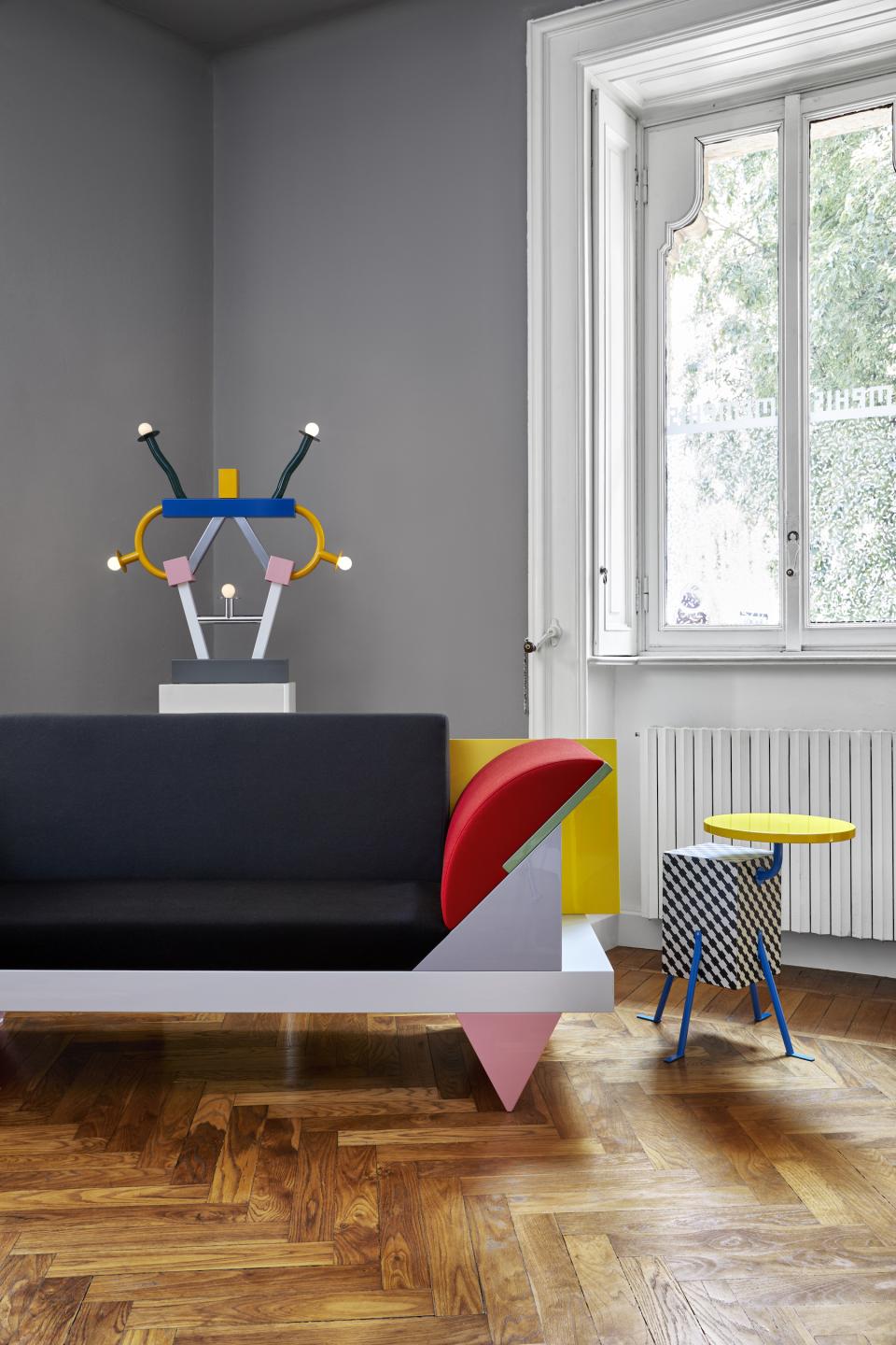 Colorful Memphis Milano-inspired furniture arrangement featuring a geometric sofa, unique lamps, and a side table in a stylish interior.