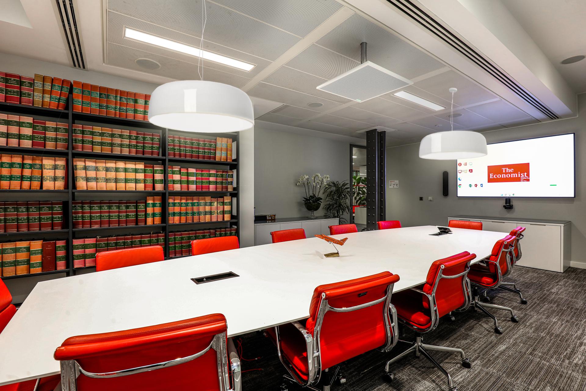 Modern conference room featuring red chairs, a large white table, and historic bookshelves for The Economist Group's sustainable design project.