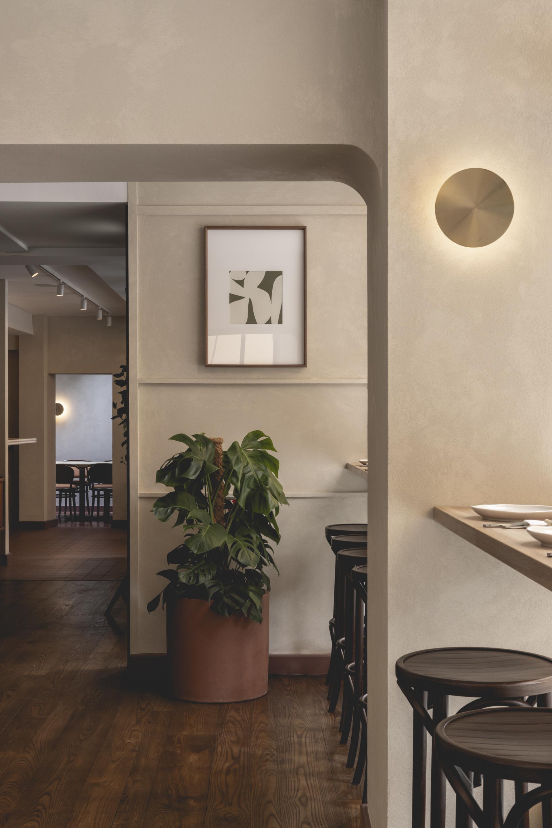Interior of Honey & Co Bloomsbury, featuring modern decor, plants, and artistic wall framing in a cozy dining atmosphere.