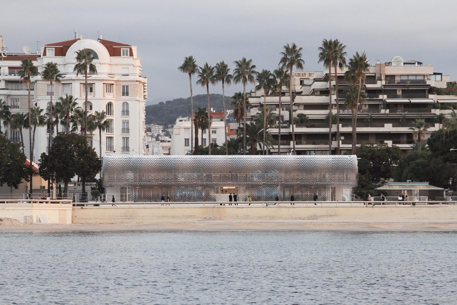 Contemporary architectural design featuring a reflective, fish-scale structure by Giles Miller Studio near a beachside promenade.