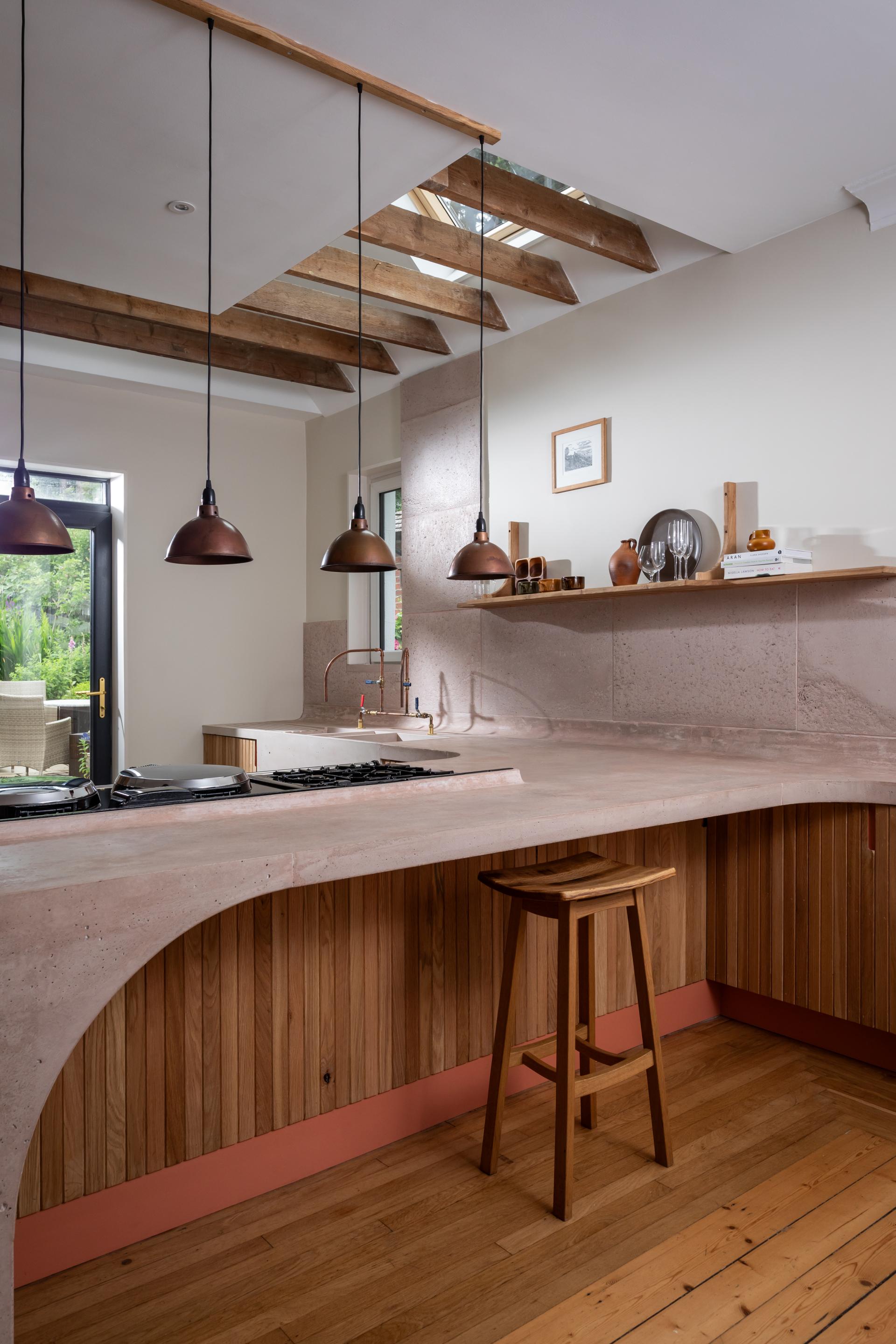 Modern kitchen featuring poured pink concrete countertops, Scottish Oak cabinetry, and stylish pendant lighting, designed by Nicholas Denney Studio.