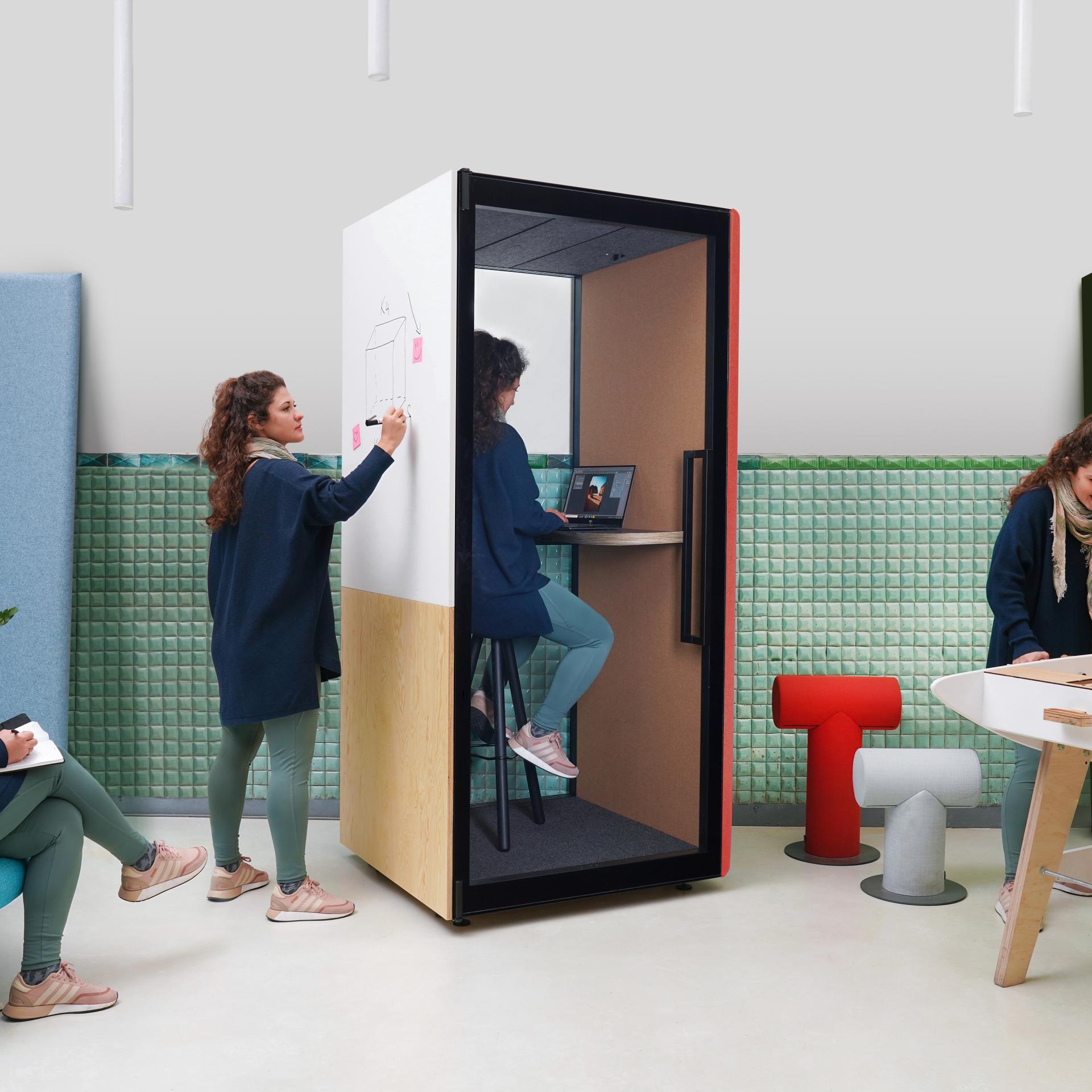 A creative workspace featuring a design booth, a woman sketching ideas, and colorful furniture at Clerkenwell Design Week.