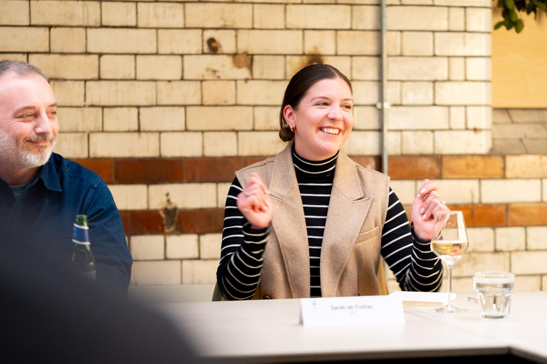 A woman smiles and gestures enthusiastically during a discussion on EDI, seated beside a man at a table.