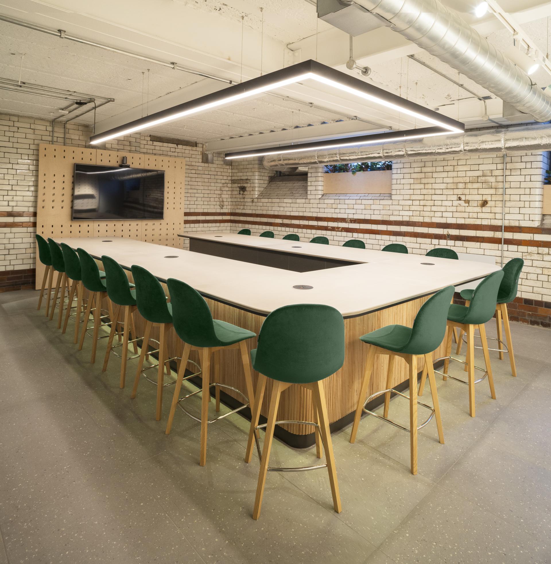 Modern meeting room in Material Source Studio, featuring a large table, green bar stools, and contemporary lighting design.