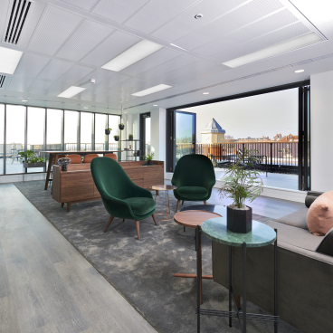Modern office interior designed by SpaceInvader featuring green chairs, natural decor, and large windows overlooking Windsor.