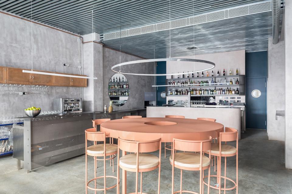 Interior of a modern Seville restaurant featuring a concrete design, circular pink table, and vibrant bar shelving.