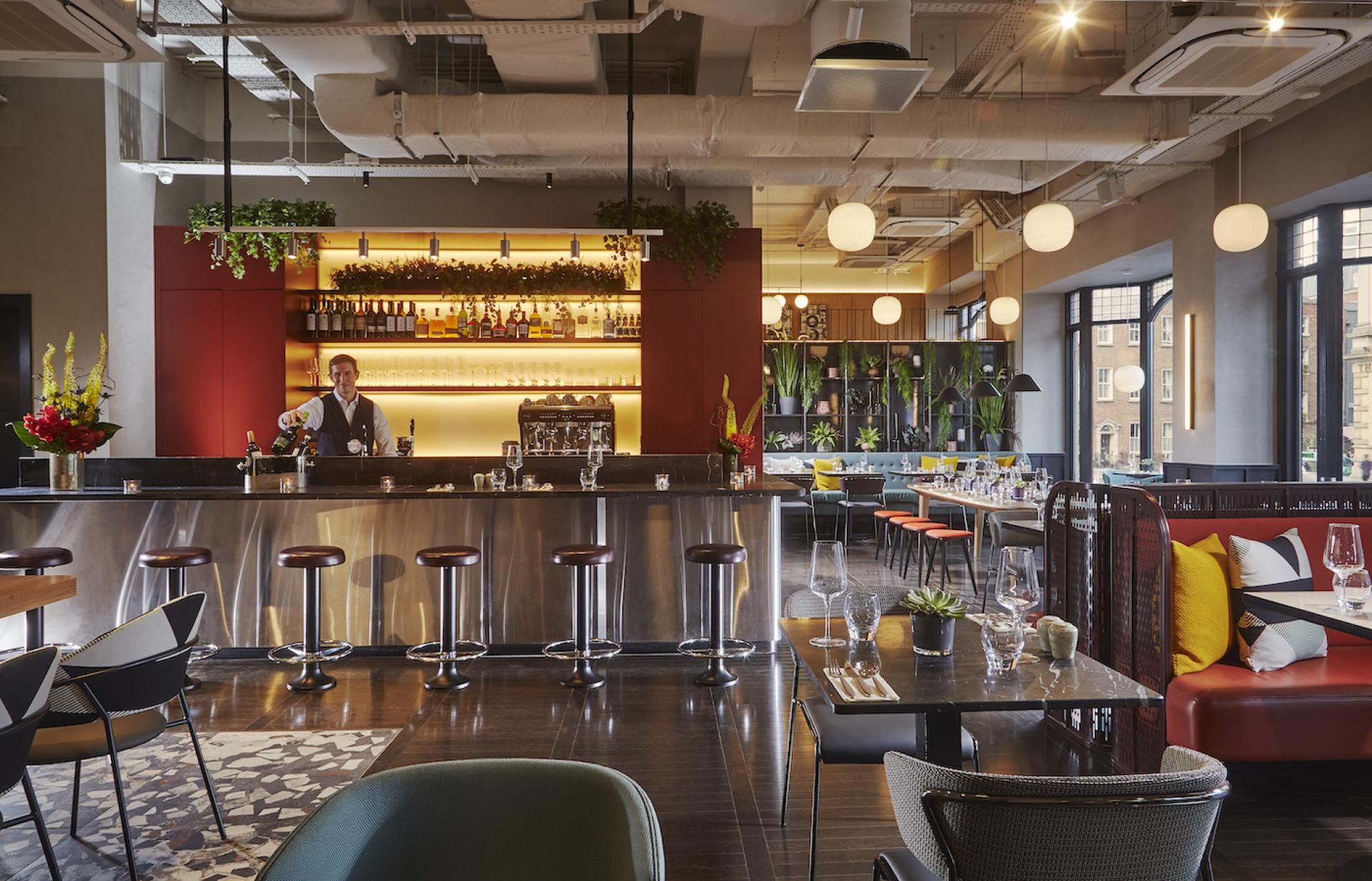 Stylish bar area of The Mont Hotel in Dublin featuring modern decor, a bartender, and vibrant seating.