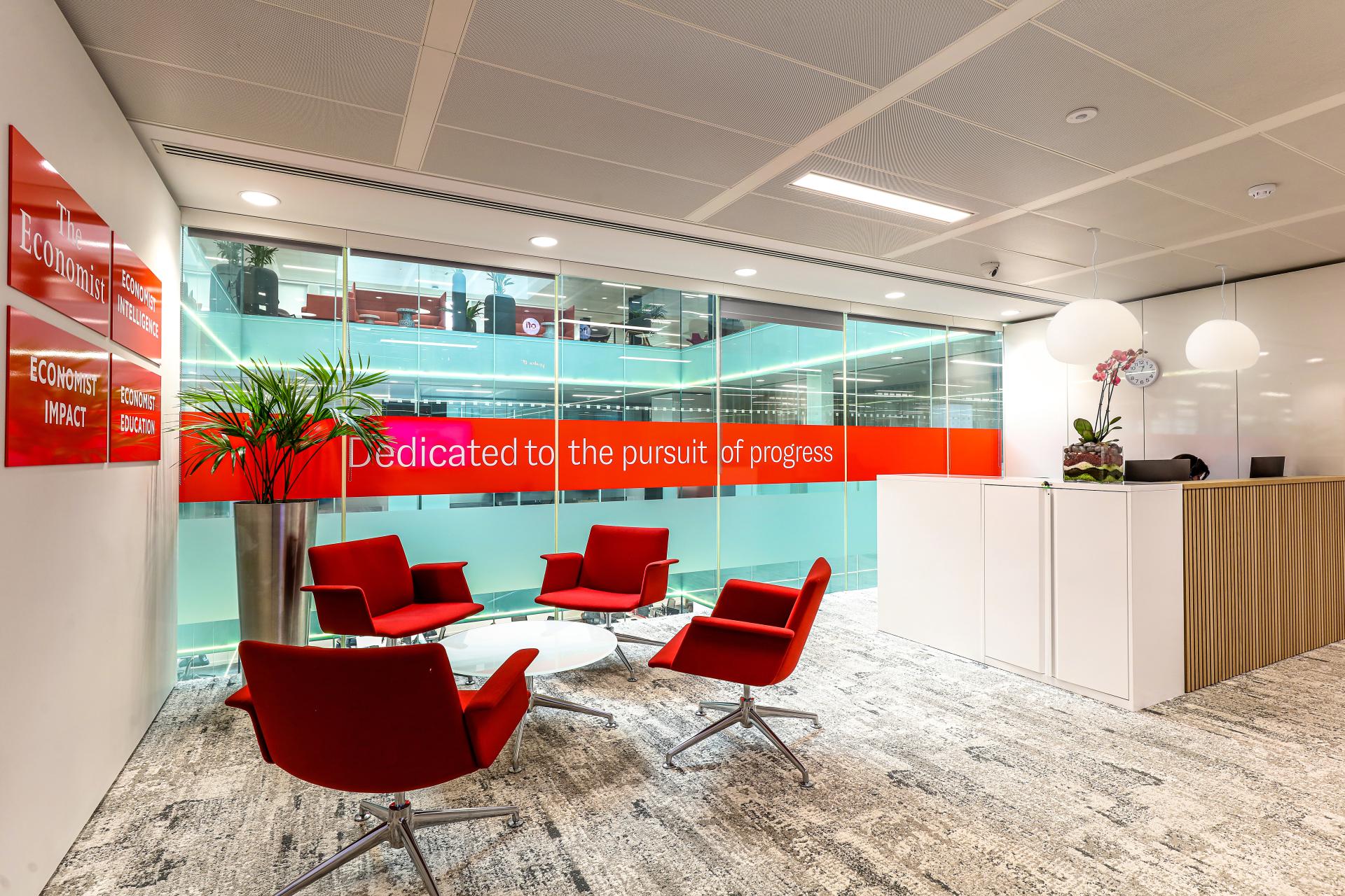 Modern office reception featuring red chairs and glass wall with the phrase 'Dedicated to the pursuit of progress.'