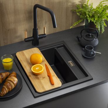 Stylish sink from Abode's Synchronist collection with fruit, croissants, and a modern faucet on a sleek countertop.