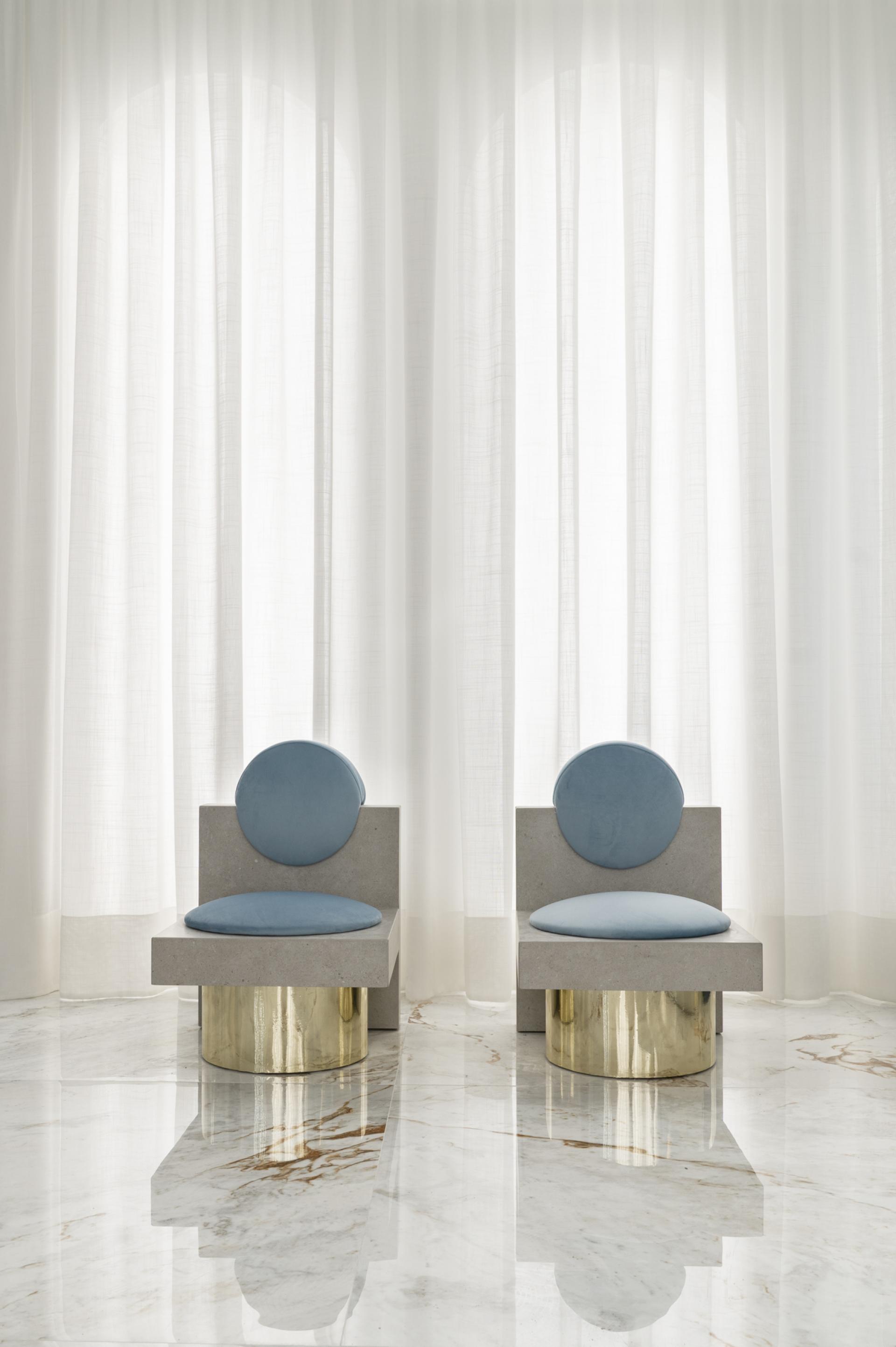 Contemporary ceramic chairs with rounded backs, set against white curtains in a modern interior design space.