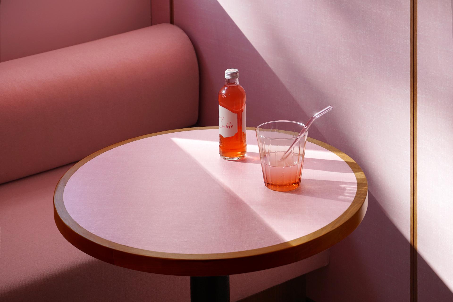 A stylish, pink café table setting featuring a drink and soda bottle, embodying 1950s design nostalgia.