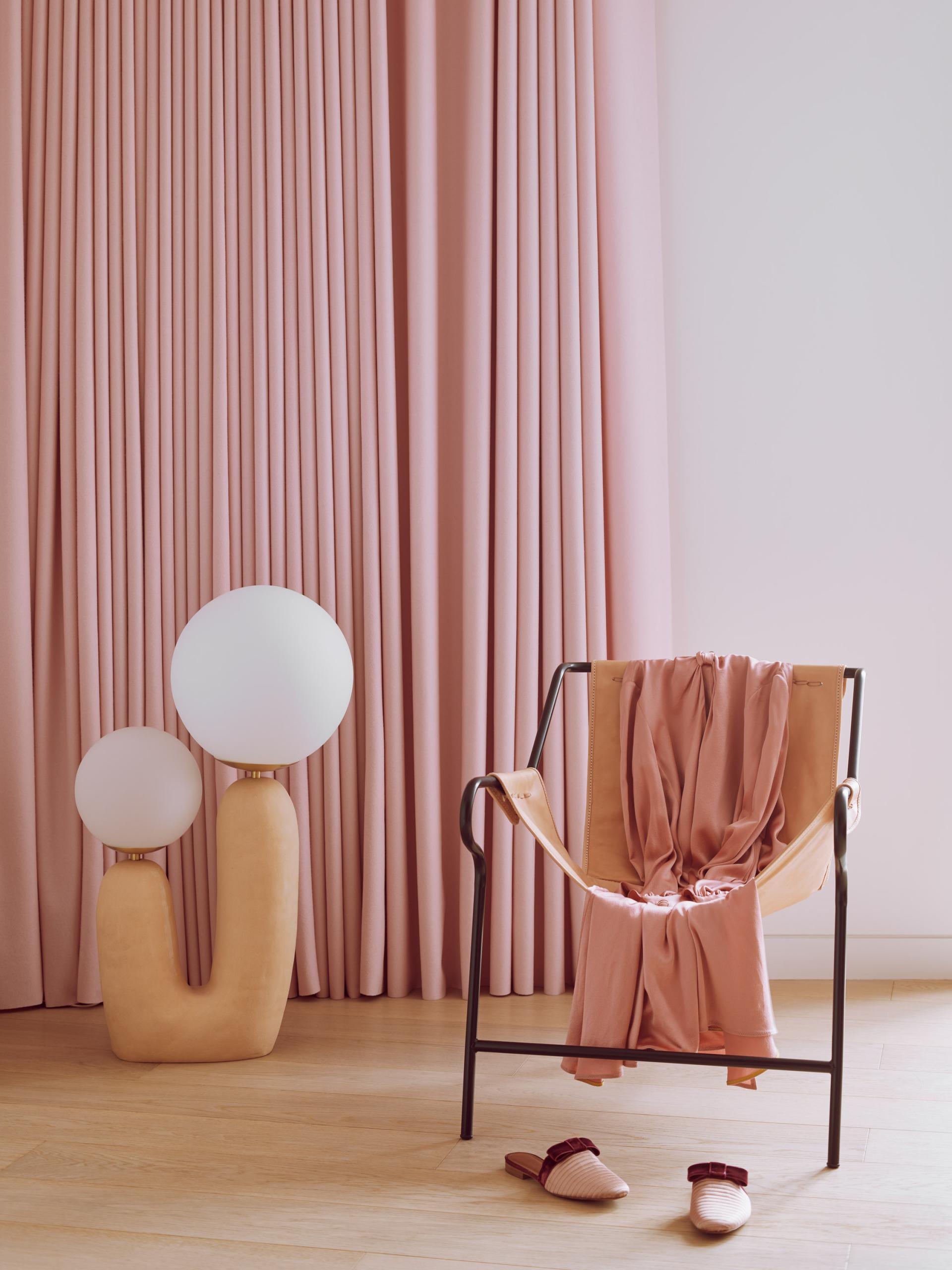 Stylish pink curtains frame a modern chair draped with fabric and a playful lamp, showcasing Roksanda's interior design aesthetics.