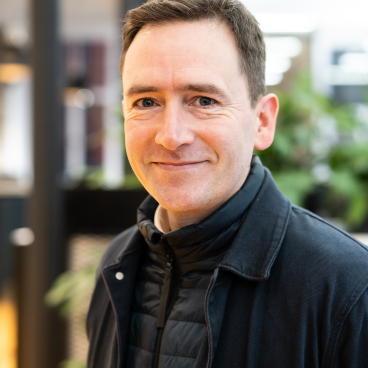 Architect Edward Dymock smiles while discussing Glasgow's Net Zero journey and sustainable design strategies in an indoor setting.