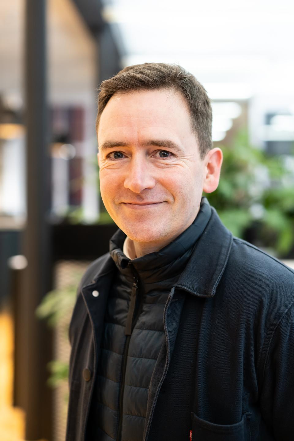 Architect Edward Dymock smiles while discussing Glasgow's Net Zero journey and sustainable design strategies in an indoor setting.