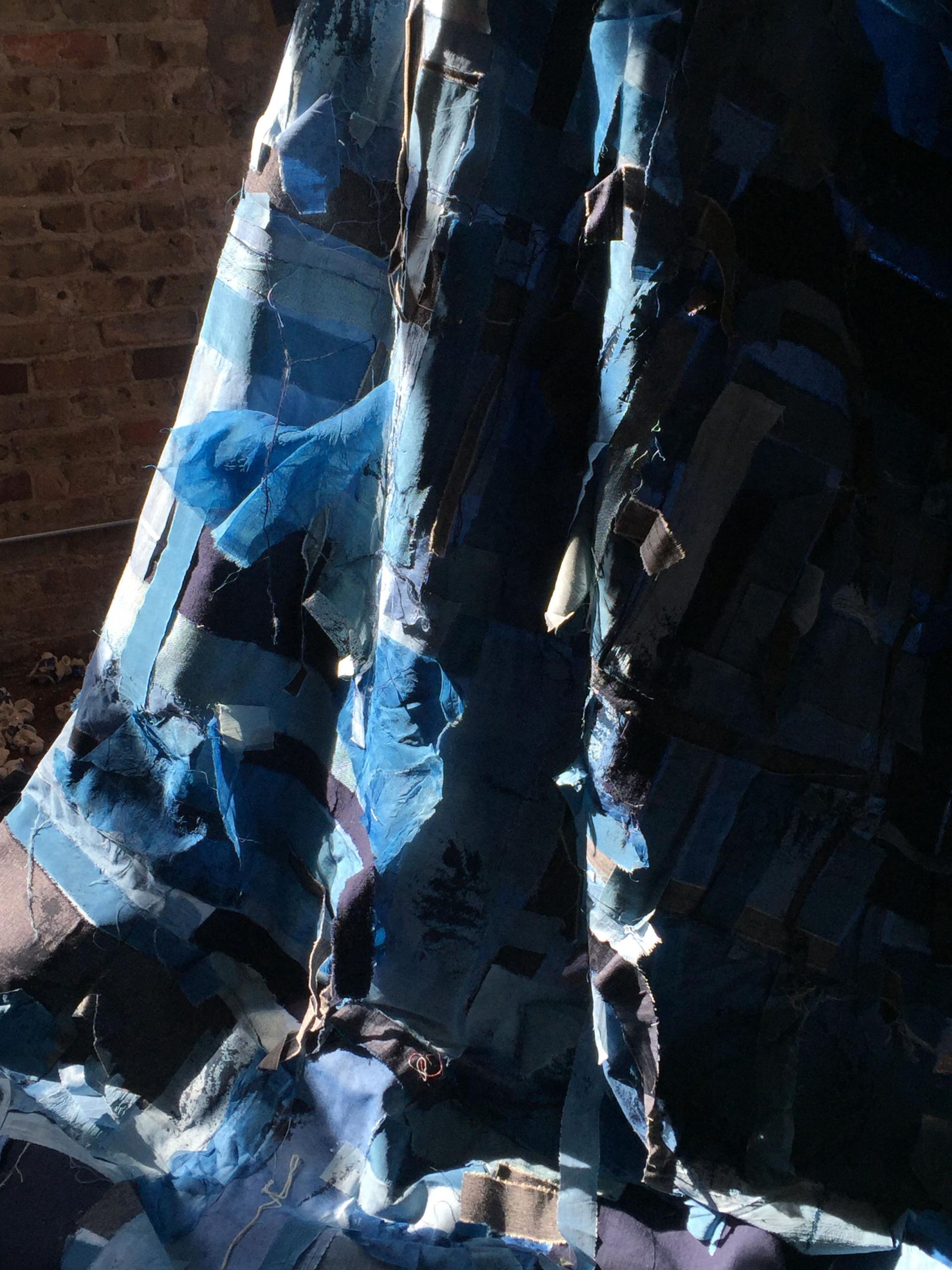 Textile artwork featuring various shades of indigo fabric, highlighting the labor-intensive process of indigo dye production.