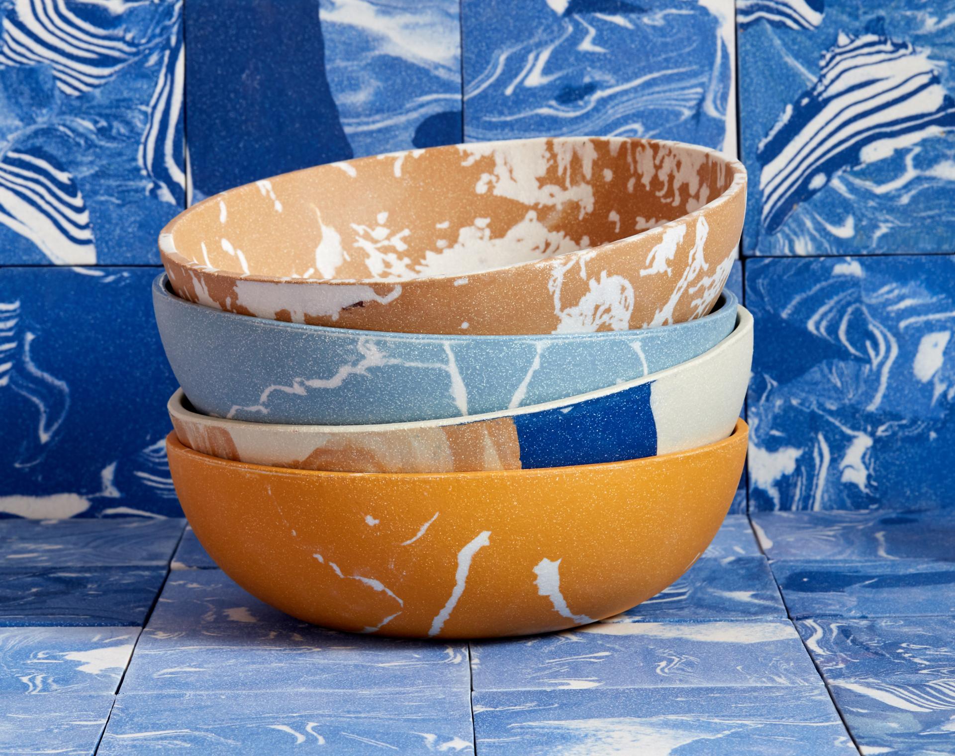 Colorful encaustic bowls stacked against a backdrop of blue patterned tiles, showcasing Granby Workshop's new tableware designs.
