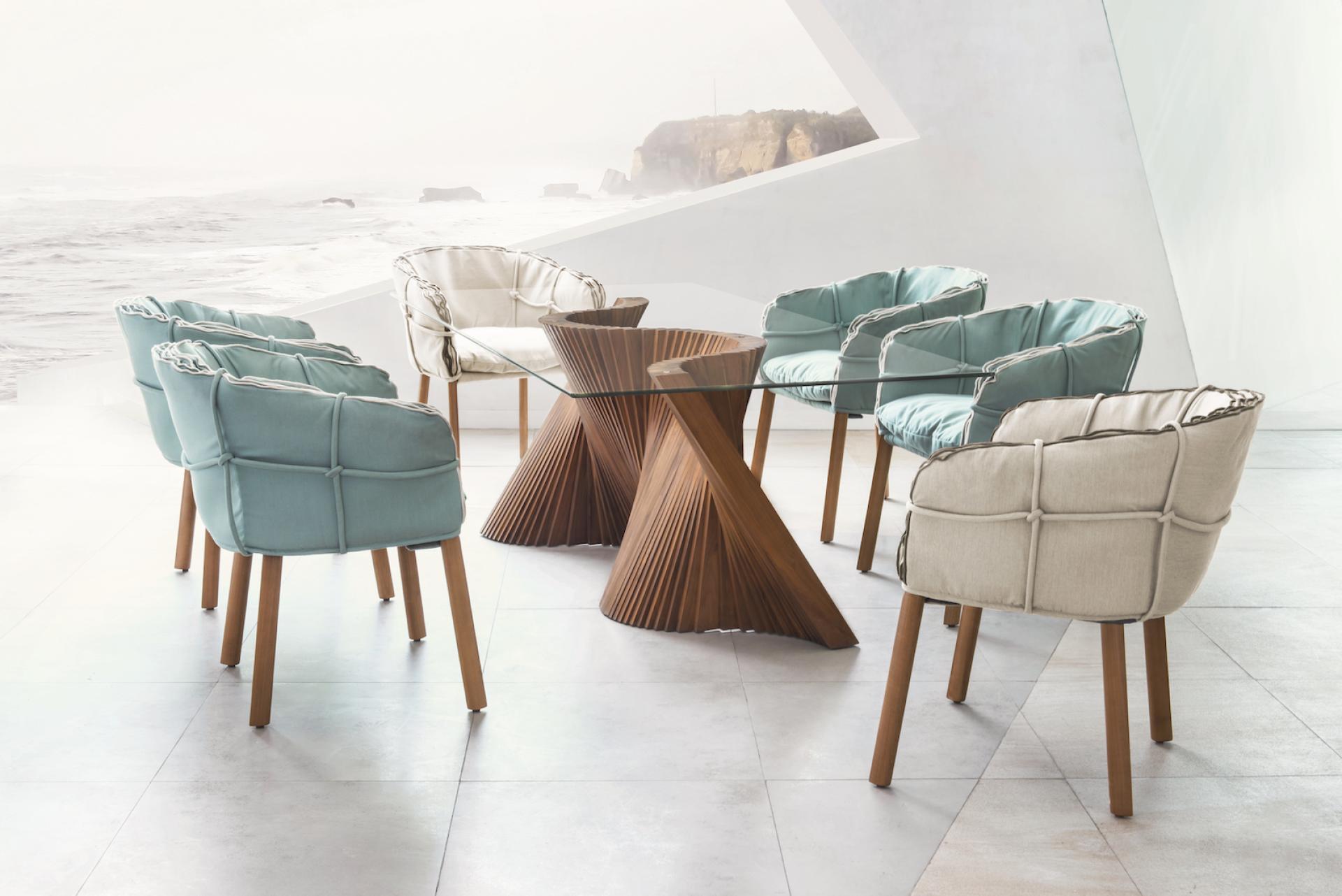 Elegant Parchment seating collection by Kenneth Cobonpue featuring plush chairs and a sculptural wooden table, set by the ocean.