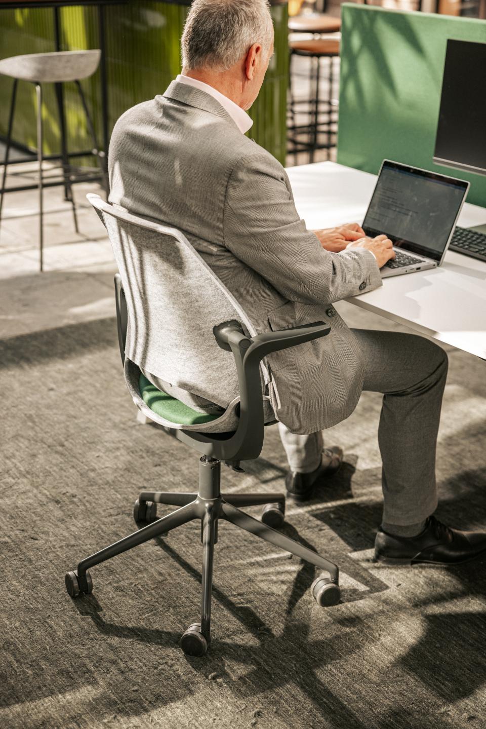 A professional seated in a Vepa Be Hybrid task chair, using a laptop in a modern office environment.