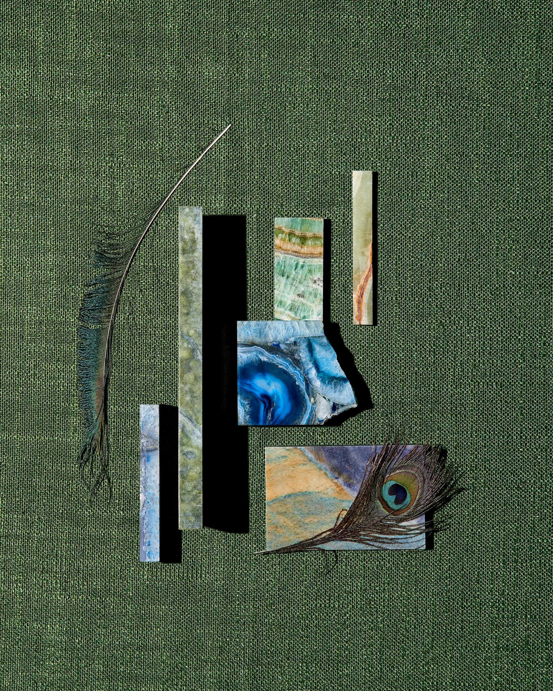 Natural stones and a peacock feather artfully arranged on green fabric, showcasing SolidNature's Green Stone Collection.