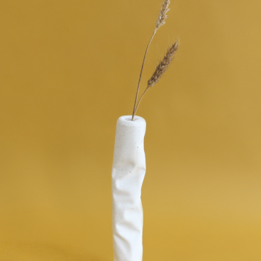 Modern white ceramic vase with textured surface, holding dried grasses against a warm yellow background.