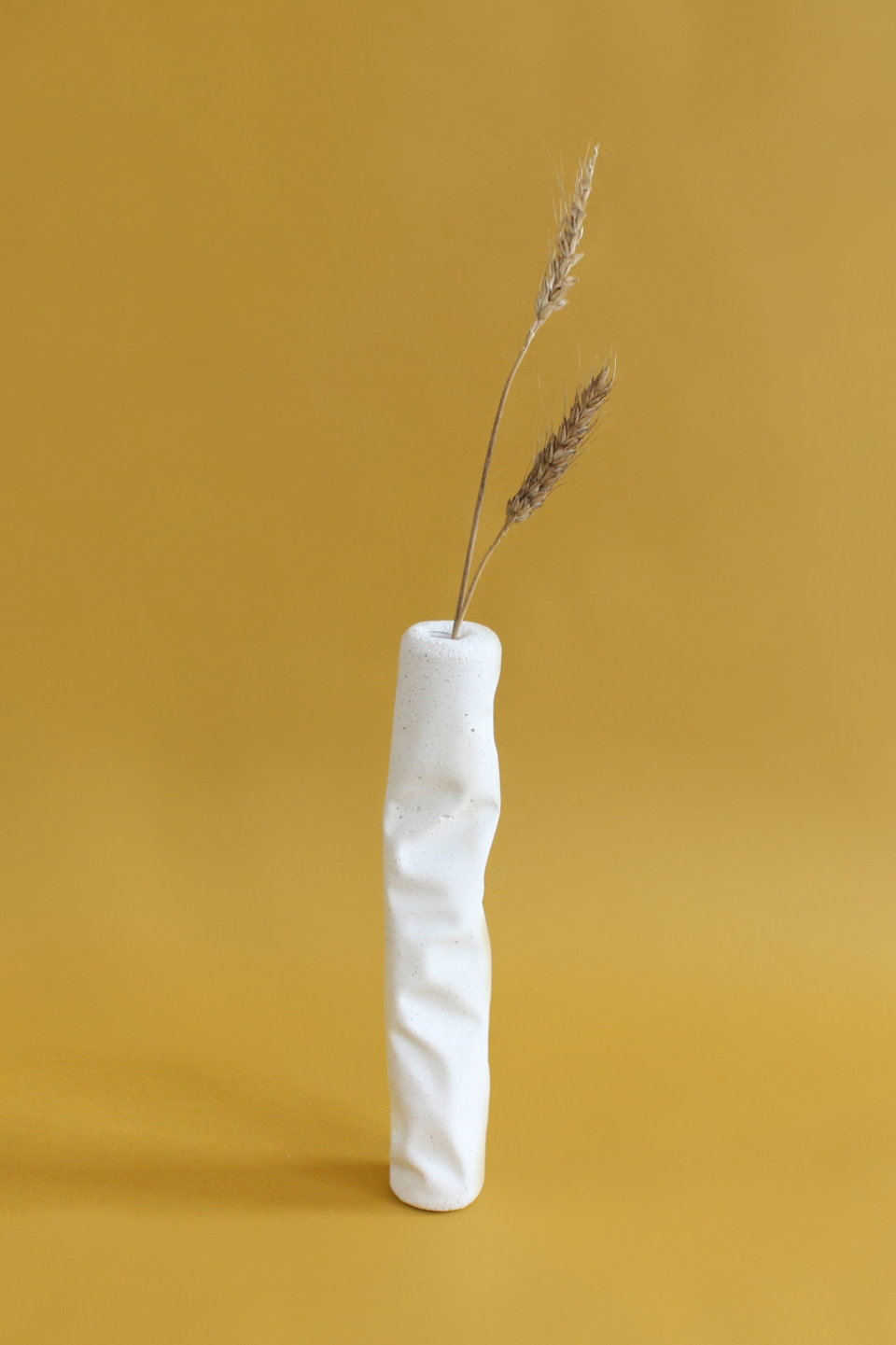 Modern white ceramic vase with textured surface, holding dried grasses against a warm yellow background.