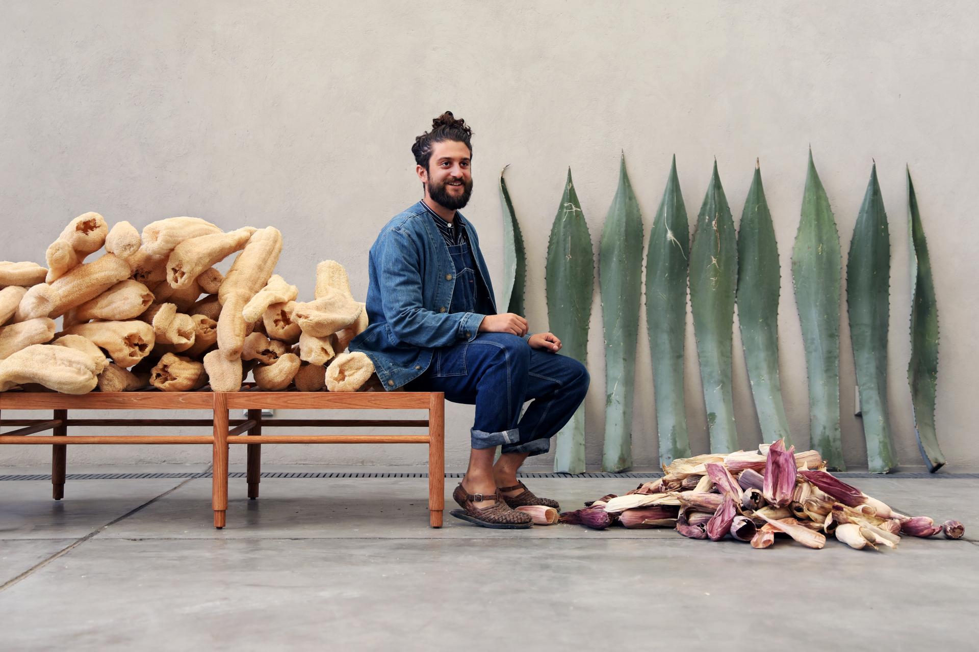 Man sitting beside vibrant corn husks and agave leaves, showcasing sustainable materials for the Totomoxtle project.